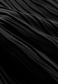 Tessuto nero con una texture ondulata a diverse profondità, che mostra pieghe sottili e linee morbide su tutta la sua superficie.