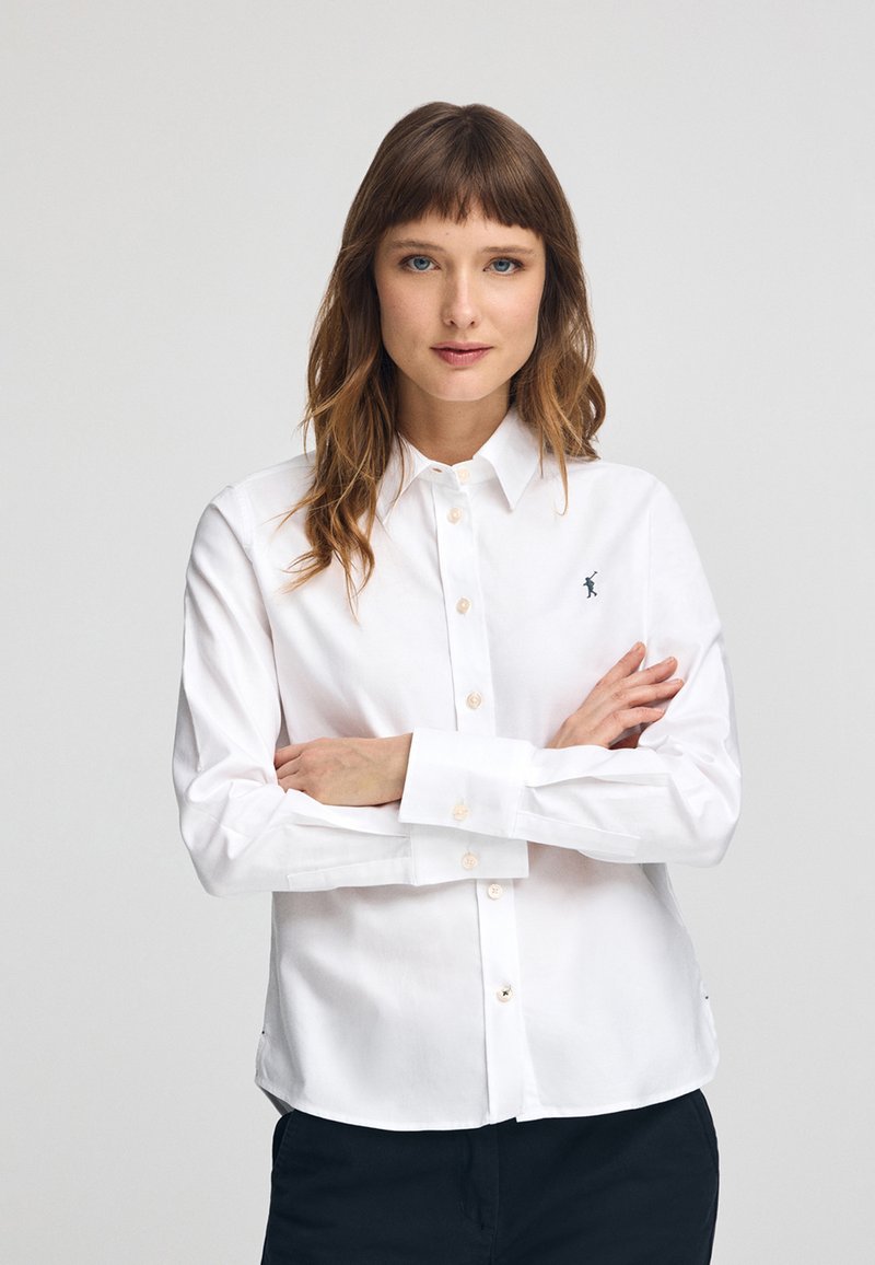 Camicia bianca con bottoni realizzata in cotone, con maniche lunghe, colletto classico e un piccolo logo ricamato sul lato sinistro del petto.