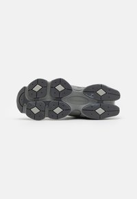 Semelle d'une chaussure New Balance grise montrant un motif de gomme noire et grise avec des motifs d'adhérence en forme de losange.