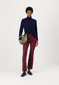 Suéter de cuello alto azul marino, pantalones acampanados burdeos y un bolso de hombro verde. Unos mocasines negros completan el conjunto sobre un fondo liso.