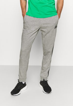 Pantalones deportivos grises de tela suave, con franjas laterales negras y puños acanalados. Combinados con zapatillas negras y una camiseta verde.