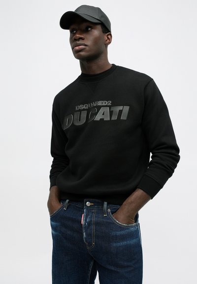 Zwarte sweatshirt met reliëftekst "DSQUARED2" en "DUCATI", gecombineerd met donkerblauwe jeans met een subtiele wassing en label op de zak.