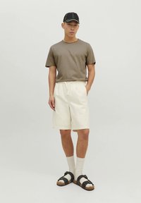 Ležérny outfit pozostávajúci z olivovo zelenej trička s krátkym rukávom, krémových šortiek, čiernych sandálov so sponou a bielych členkových ponožiek.