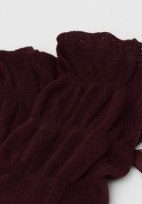 Burgundyröd stickad benvärmare med ribbstruktur och volangkant. Mjuk material med ett enhetligt stickmönster.
