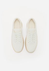 Baskets blanches avec un dessus en cuir lisse, des lacets plats, un bout rond et une semelle en caoutchouc beige. Design minimaliste avec des accents discrets.