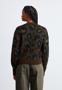 Bruine trui met groene en zwarte luipaardprint, voorzien van een ribgebreide zoom en lange mouwen. De achterkant toont de gemêleerde stof.