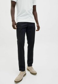 Zwarte rechte broek van katoen, gecombineerd met lichtbeige suède schoenen. De pasvorm is casual, geschikt voor dagelijks gebruik.