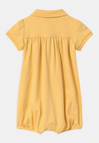 Žlutý bavlněný dětský overal s polo límečkem, krátkými rukávy, nařaseným pasem a elastickým lemem pro pohodlný střih.