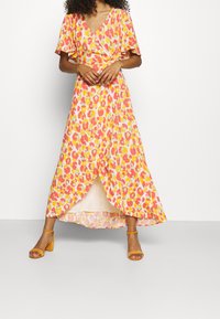 Maxiklänning i livlig rosa, gul och orange leopardmönster, med omslagdesign, fladdrande ärmar och en slits fram.