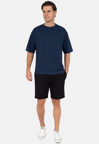 Marineblauw katoenen T-shirt met korte mouwen, gecombineerd met zwarte korte broek. Witte sneakers met rode accenten maken de outfit compleet.