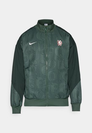 Casaco verde da Nike com fecho total, apresenta tecido texturizado com padrões de letras repetidas, mangas em contraste e um logotipo de leão vermelho.