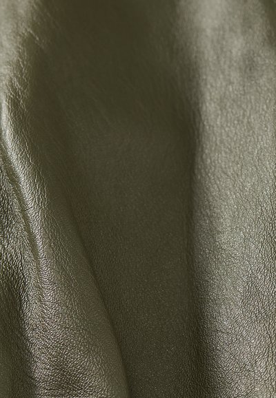 Κοντινό πλάνο σκουρόχρωμου πράσινου γυαλιστερού δερμάτινου υφάσματος που δείχνει τη υφή και τις φυσικές ρυτίδες.