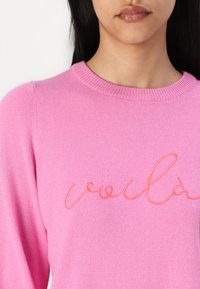 Pull rose avec un col rond. Présente une texture douce et brodée "voilà" dans une teinte de rose plus claire. Manches longues.