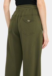 Pantaloni tuta verde con vita elasticizzata a coste, tasche laterali e un dettaglio decorativo in hardware dorato sulla tasca posteriore.