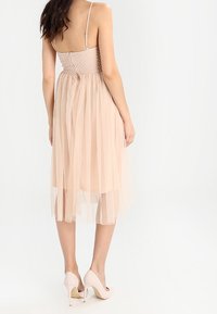 Růžové tylové šaty s přiléhavým smockovaným živůtkem a tenkými ramínky, s vrstvenou, sukní ke kolenům a doplněné béžovými lodičkami.