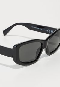 Black rectangular sunglasses with dark tinted lenses, thicker arms, and a glossy finish. Slight curves at the edges, minimal hardware details.