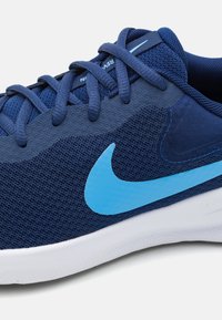 Marineblauwe sportschoen met mesh en synthetisch materiaal, een lichtblauwe swoosh-logo en gestructureerde details op de bovenkant. Witte zool.