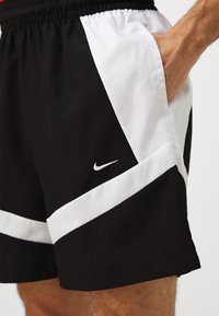 Black and white athletic shorts featuring a drawstring waistband, side pockets, and a small Nike logo on the lower left.