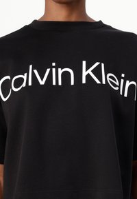 Black cotton T-shirt featuring a large, white "Calvin Klein" logo across the chest. Crew neckline with short sleeves. Smooth texture.