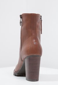 Bottillons en cuir marron avec une fermeture éclair, bout rond et un talon épais et cranté. Présente une petite étiquette de logo à l'arrière.