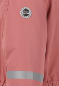 Veste rose clair avec un logo gris rond portant le texte "ZIGZAG", bande réfléchissante grise le long de la manche, fabriquée en tissu lisse et texturé.