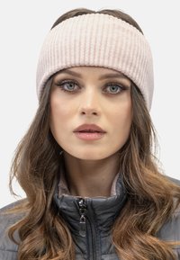 Bandă de cap tricotată ribbed de culoare roz deschis, realizată dintr-un material moale, cu un bandaj lat. Purdată cu o jachetă gri închis cu fermoar. Textură netedă.