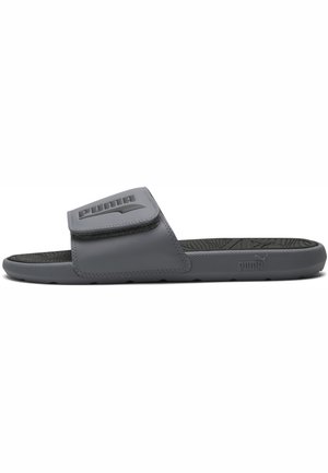 Sandalia tipo slide gris de Puma con tira ajustable, plantilla texturizada y logo de Puma en la tira y en el lateral de la suela.