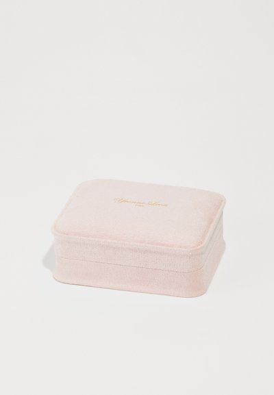 Pink velvet jewelry box with a rectangular shape, rounded edges, and a gold embossed logo on the top. Soft texture, no visible hardware.