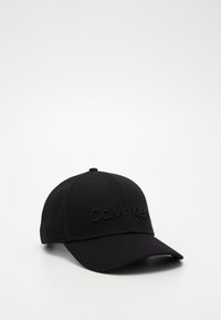 Casquette de baseball noire en tissu au toucher lisse. Présente un logo "Calvin Klein" brodé à l'avant. Design classique avec visière courbée.