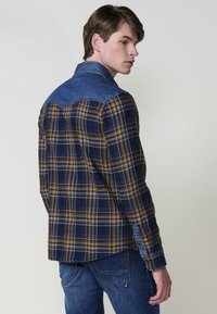 Kockás flaneling kék farmer yokkal, sárga és sötétkék kockamintával, gombos mandzsettákkal és egyenes szabással.