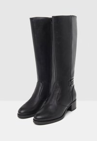 Bottes noires en cuir haute jusqu'au genou avec une texture lisse, fermeture par zip sur le côté, talon bloc bas et détail d'accent métallique.