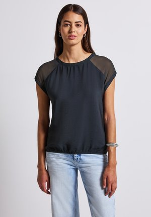 Top nero con maniche corte, dettagli in tessuto trasparente sulle spalle, vestibilità rilassata, scollatura rotonda e finitura testurizzata; abbinato a jeans azzurri chiari.