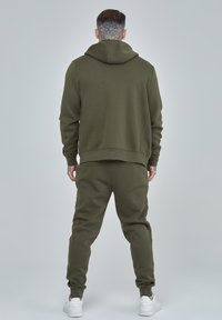 Conjunto de sudadera y pantalones de chándal en verde oliva, hecho de material suave, con un corte relajado, puños acanalados y un bolsillo tipo canguro en la sudadera.