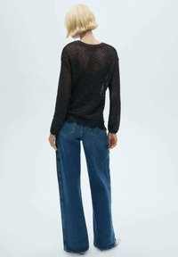 Maglione nero a maniche lunghe in maglia con vestibilità ampia, abbinato a jeans blu a vita alta e gamba larga con tasche posteriori e cuciture discrete.