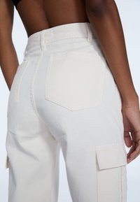 Hvide cargo-bukser lavet af bomuld, med store baglommer og sidelommer. Glat tekstur med kontraststing detaljer.