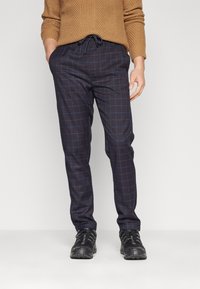 Marinblå rutiga byxor med blå linjer, tillverkade av ett slätt tyg. Elastisk dragsko i midjan, kombinerade med svarta utomhusskor.