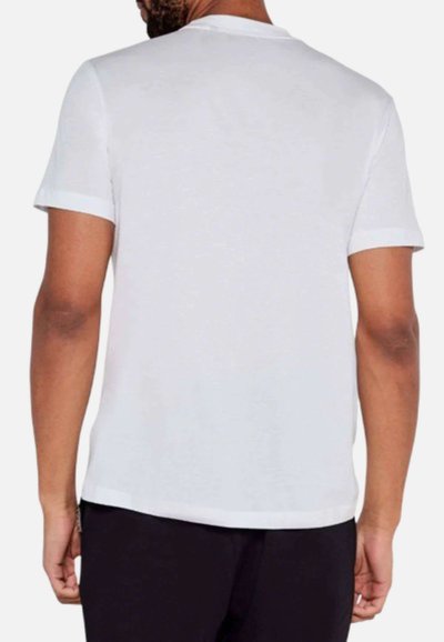 Camiseta blanca de manga corta con cuello redondo y dobladillo recto. Textura suave con puños doblados, vista desde la parte de atrás.