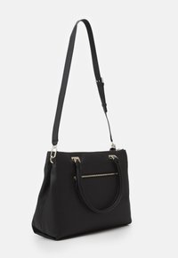 Sac en cuir noir avec deux poignées courtes, une bandoulière longue réglable et une poche zippée à l'avant, présenté sur un fond blanc.