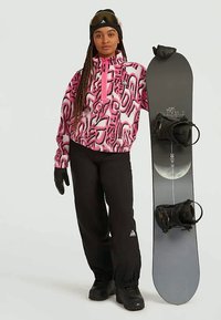 Fleece-pullover i pink og hvid swirl mønster; sorte bukser; holder et snowboard med sorte bindinger; sorte handsker og skibriller.
