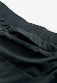 Mørke stofshorts med et struktureret mønster og elastisk talje. Har en lynlåslomme til sikker opbevaring.