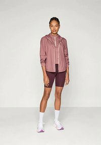 Kerge lavendlitootel sportlik jakk valge tõmblukuga, kombineeritud sobiva ülevalt ja tumepunaste jalgrattashortsidega. Jalatsite disain sisaldab valgeid ja roosa aktsente.