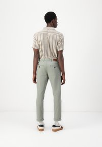 Chemise à manches courtes rayée dans des tons beige et marron, assortie à un pantalon vert clair, avec des poignets retroussés et un détail en patch de cuir marron.