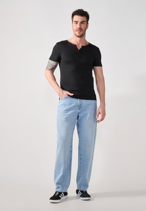 Zwarte t-shirt met korte mouwen en een ronde hals, gecombineerd met lichtblauwe rechte jeans en zwarte sneakers met witte zolen.