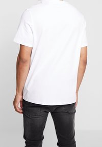 Bílý krátký rukávový tričko vyrobené z bavlny, s kulatým výstřihem, volným střihem a hladkou texturou. Následuje s tmavými džínami.