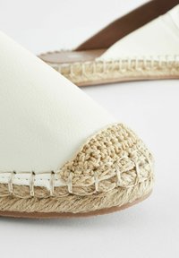 Vit faux-läder espadrillo med vävt jute- och repdetalj vid tån. Platt sula och rund form. Strukturerad yta.
