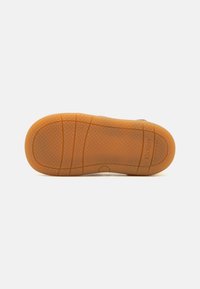 Brązowy kauczukowy spód buta z teksturowanym, kropkowanym wzorem, z zaznaczonymi bruzdami i okrągłym detalem w pobliżu środka. Wytłoczone logo "Kickers".