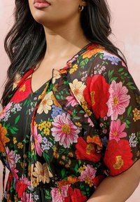 Mustaharhoti musta kukkakuvioinen mekko, jossa on eloisat punaiset, vaaleanpunaiset ja keltaiset kukat. Kevyt kangas, rypyttyneet hihat, V-pääntie ja käänteinen vyötärö.