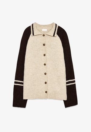 Šviesiai kreminė megzta kardiganas su tamsiai rudu raglanu. Savybė: apykaklė, septynios mygtukų priekis ir baltos juostelės akcentai ant rankovių.