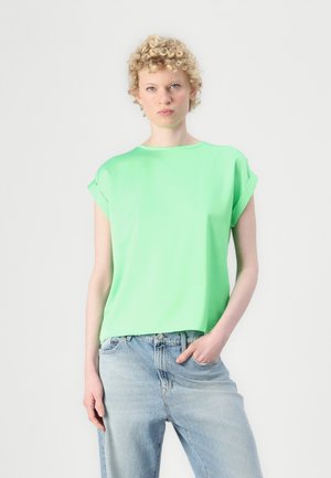 Korte ermers grønn bluse i lett stoff med løs passform. Har rullede ermer og en jevn tekstur, kombinert med lyseblå jeans.