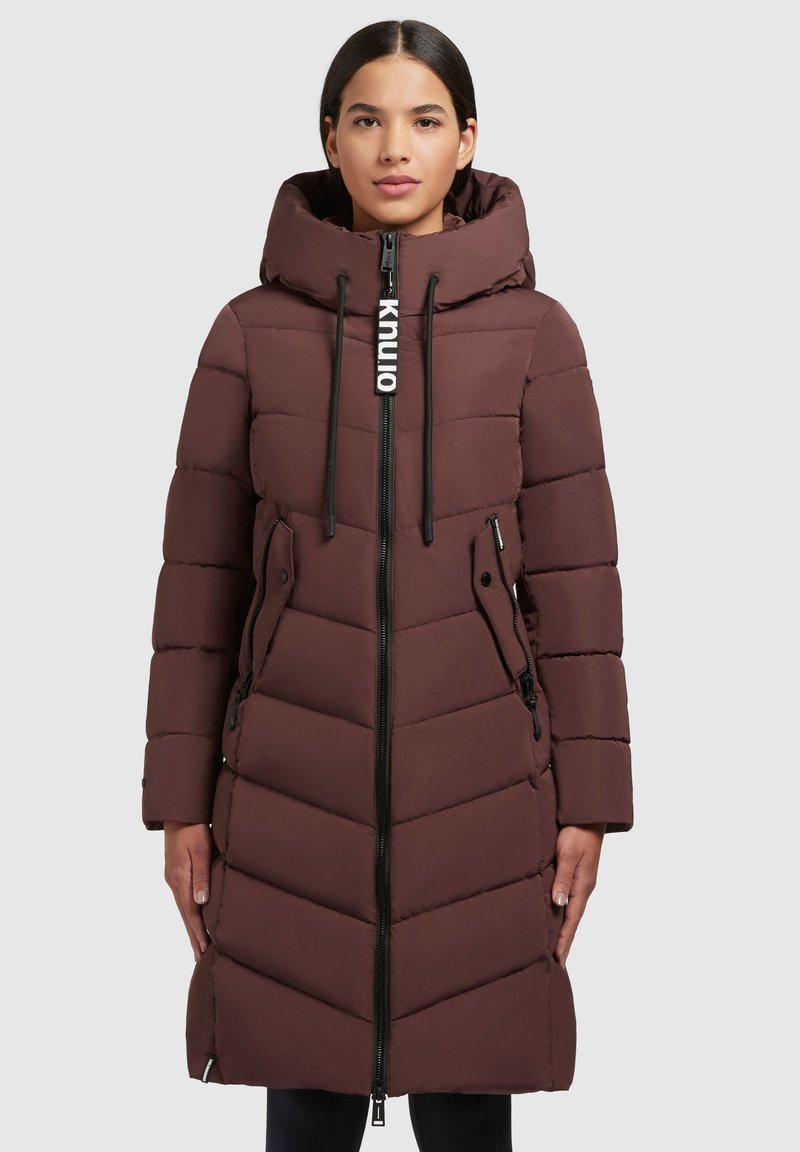 Cappotto imbottito lungo marrone con cappuccio, dotato di zip frontale, dettagli con coulisse e motivo a chevron. Tasche laterali incluse.